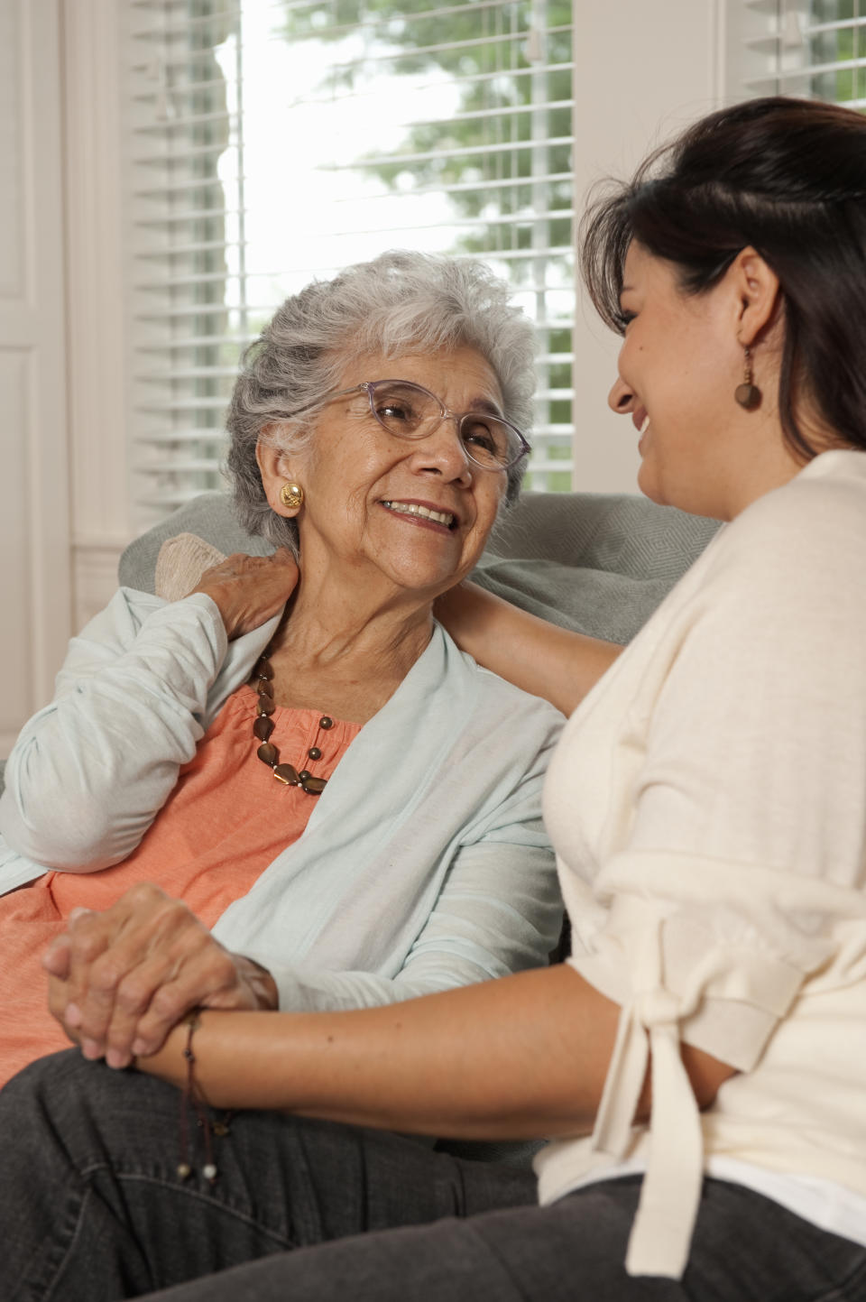 An older and younger woman holding hands on a couch.