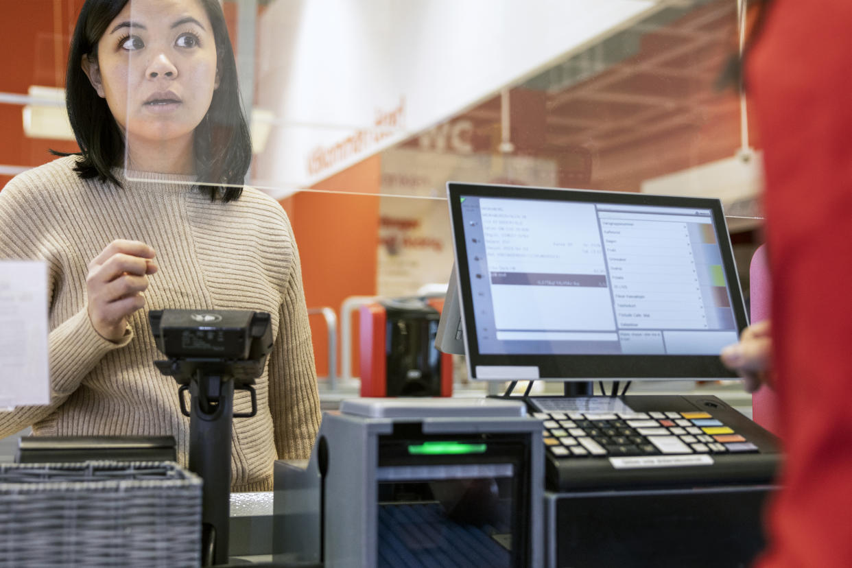 Young female customer talking to cashier at checkout in supermarket