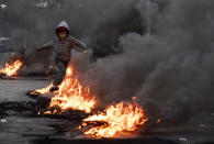 A boy jumps over burning tires that were set on fire to block a road, during a protest in Beirut, Lebanon, Tuesday, March 2, 2021. Scattered protests broke out in different parts of Lebanon Tuesday after the Lebanese pound hit a record low against the dollar on the black market, a sign of the country's multiple crises deepening with no prospects for a new Cabinet in the near future. (AP Photo/Hassan Ammar)