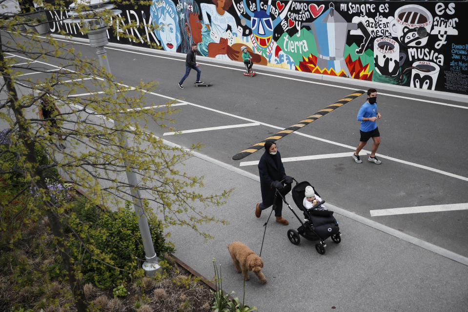 Pedestrians wearing protective masks pass through Domino Park, Friday, May 8, 2020, in the Brooklyn borough of New York. Some parks will see stepped-up policing to stem the spread of the coronavirus, New York City Mayor Bill de Blasio said Friday. He also announced that 2,500 members of a "test and trace corps" will be in place by early June to combat the virus. (AP Photo/John Minchillo)