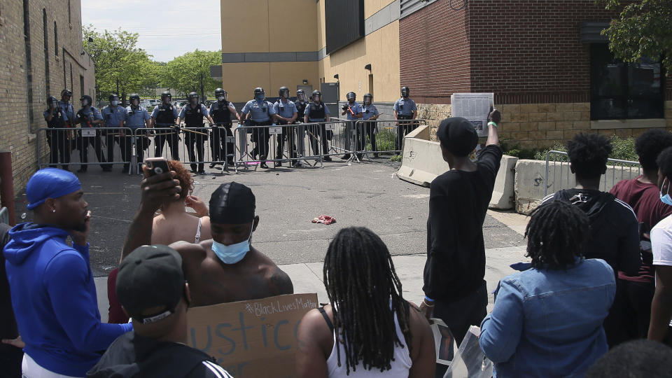 A protester holds a newspaper in front of the Minneapolis police standing guard against protesters at the Third Precinct, Wednesday, May 27, 2020, as people protest the arrest and death of George Floyd who died in police custody Monday night in Minneapolis after video shared online by a bystander showed a white officer kneeling on his neck during his arrest as he pleaded that he couldn't breathe. (AP Photo/Jim Mone)