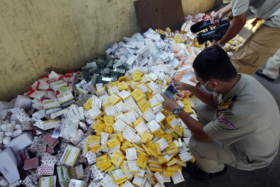 Un oficial de policía camboyano toma fotografías de pilas de medicamentos falsos antes de su destrucción en un sitio de gestión de desechos médicos en la aldea de Choeung Ek, en las afueras de Phnom Penh, Camboya, el viernes 28 de noviembre de 2014. Foto: AP / Heng Sinith.