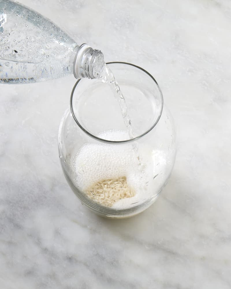 angled shot of sparkling water being poured into a vase with rice at the bottom of it.