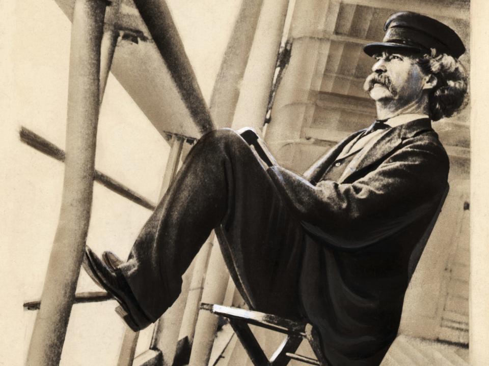 Writer Mark Twain relaxes on a ship deck with his feet on the railings.