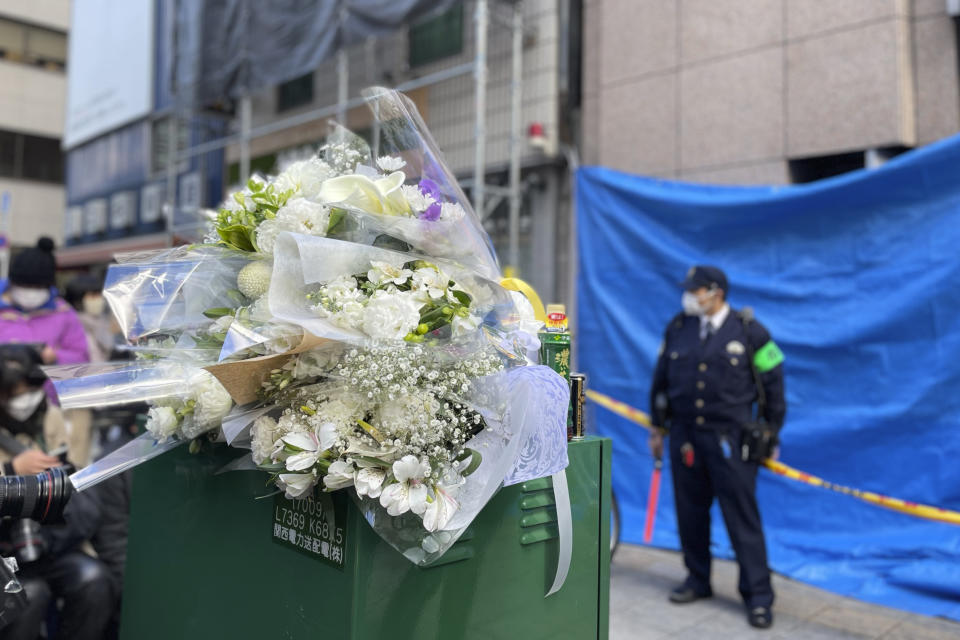 Flowers and drinks are placed in front of a building where a fire broke out Friday in Osaka, western Japan, Saturday, Dec. 18, 2021. Japanese police on Saturday searched the house of one of the patients at a mental clinic where the fire gutted an entire floor in the eight-story building, killing over 20 people trapped inside. (AP Photo/Chisato Tanaka)