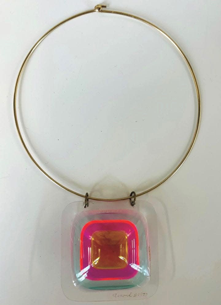 The gold necklace with a large, brightly coloured square pendant.