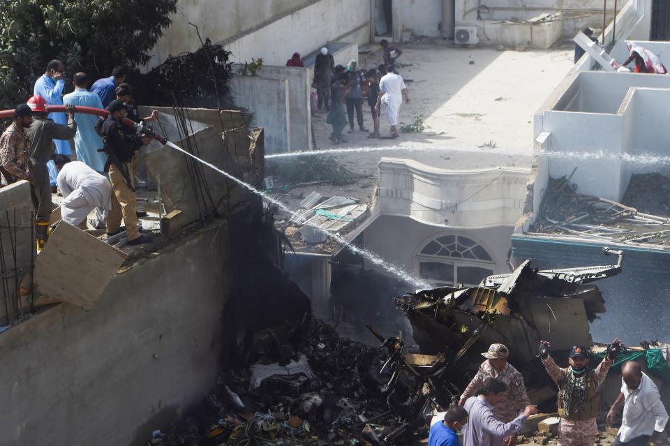 Policemen spray water on the part of a Pakistan International Airlines aircraft after it crashed at a residential area in Karachi on May 22, 2020. - A Pakistan passenger plane with more than 100 people believed to be on board crashed in the southern city of Karachi on May 22, the country's aviation authority said. (Photo by Asif HASSAN / AFP) (Photo by ASIF HASSAN/AFP via Getty Images)