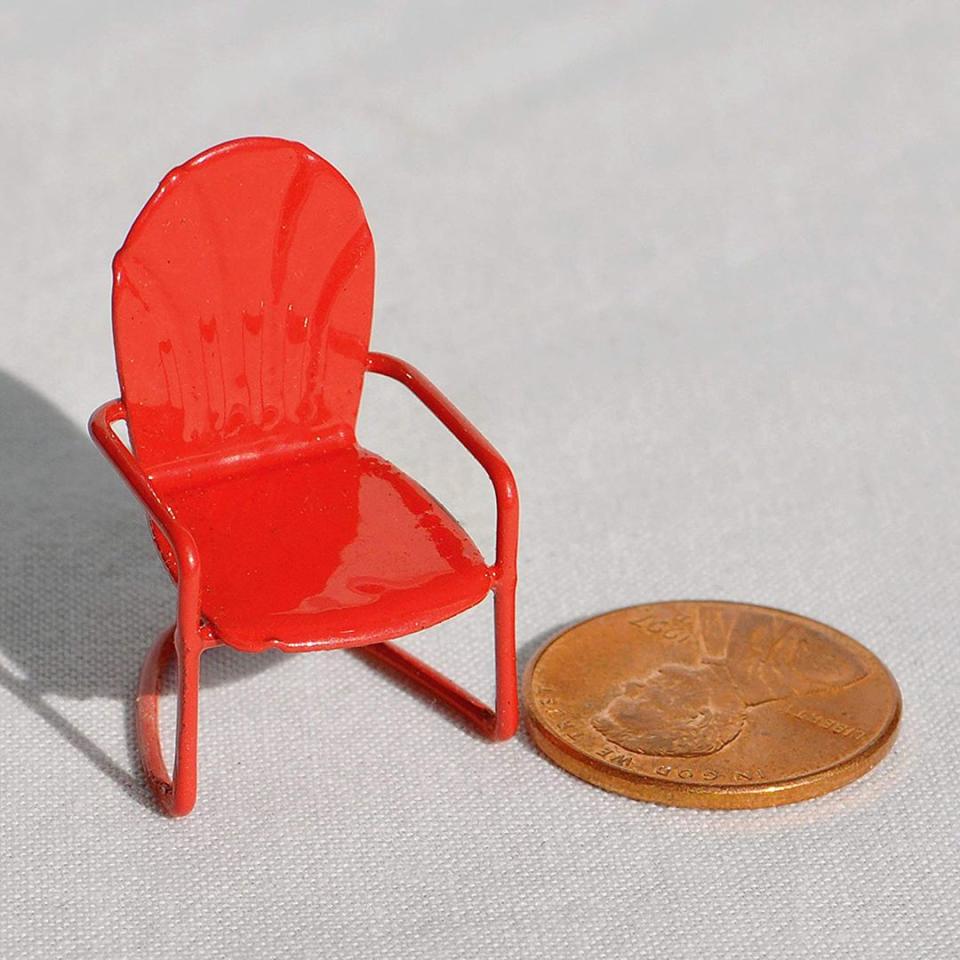 Miniature red metal lawn chair next to a penny coin for scale