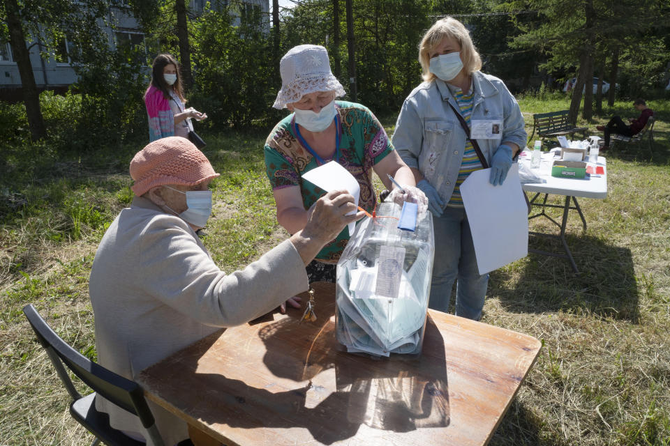 Members of the election commission wearing face masks to protect against coronavirus infection help to an elderly voter, left, to cast her ballot at an outdoor polling station in Naziya village, 80 km (50 miles) east of St.Petersburg, Russia, Sunday, June 28, 2020. Polls have opened in Russia for a week-long vote on a constitutional reform that may allow President Vladimir Putin to stay in power until 2036. (AP Photo/Dmitri Lovetsky)