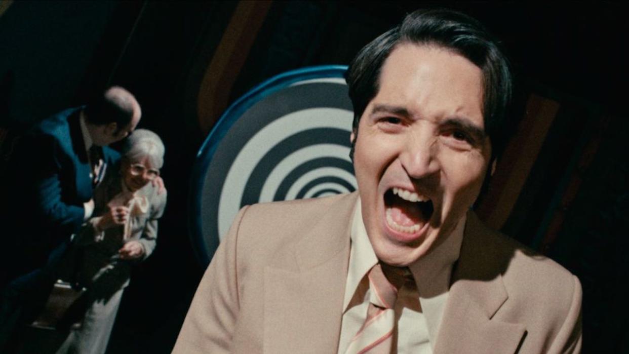  David Dastmalchian laughs maniacally in front of a hypnotic background in Late Night with the Devil. 