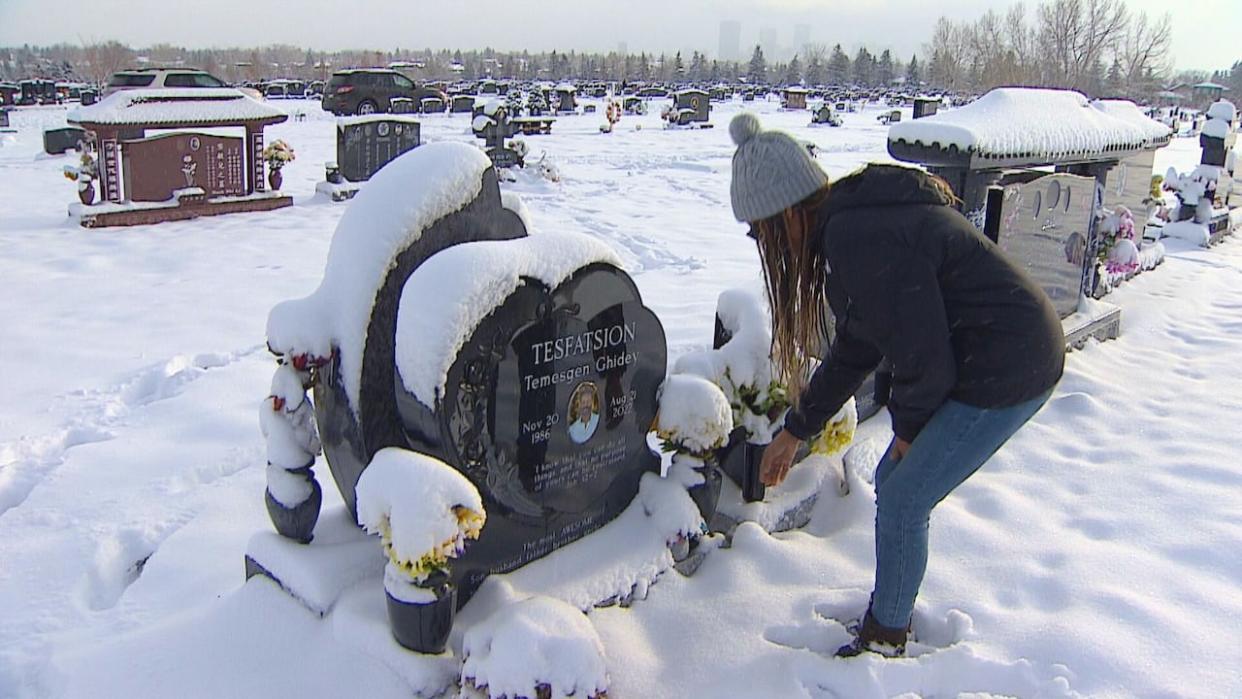 Meron Tesfatsion reaches to wipe the snow from her brother's headstone. He was killed in August 2022.  (James Young/CBC - image credit)