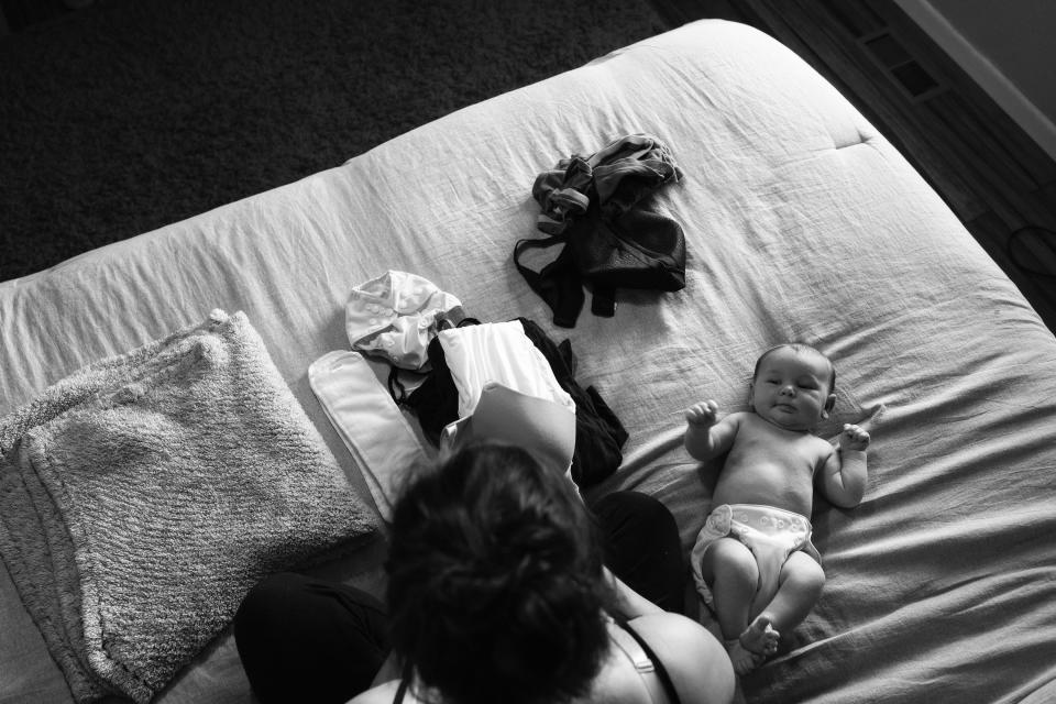 A mother folds clothes on her bed while her infant son lays next to her