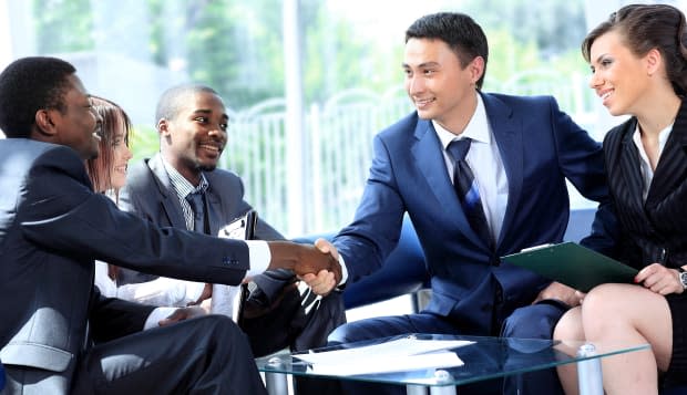 Two business man shaking hands with his team in office