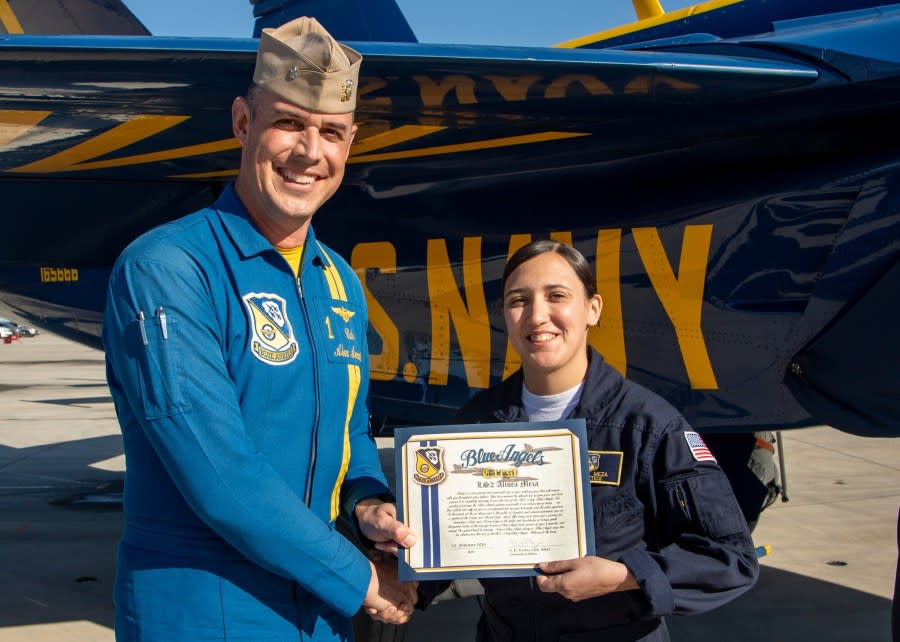 Alisea Meza holds her Blue Angels crest while shaking hands with a fellow Blue Angels member.