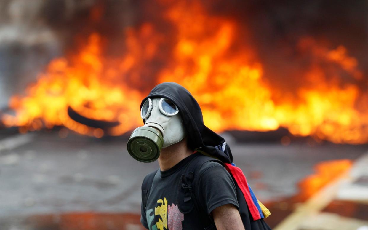 An anti-government protester stands in front of burning barricade on a highway in Caracas - AP