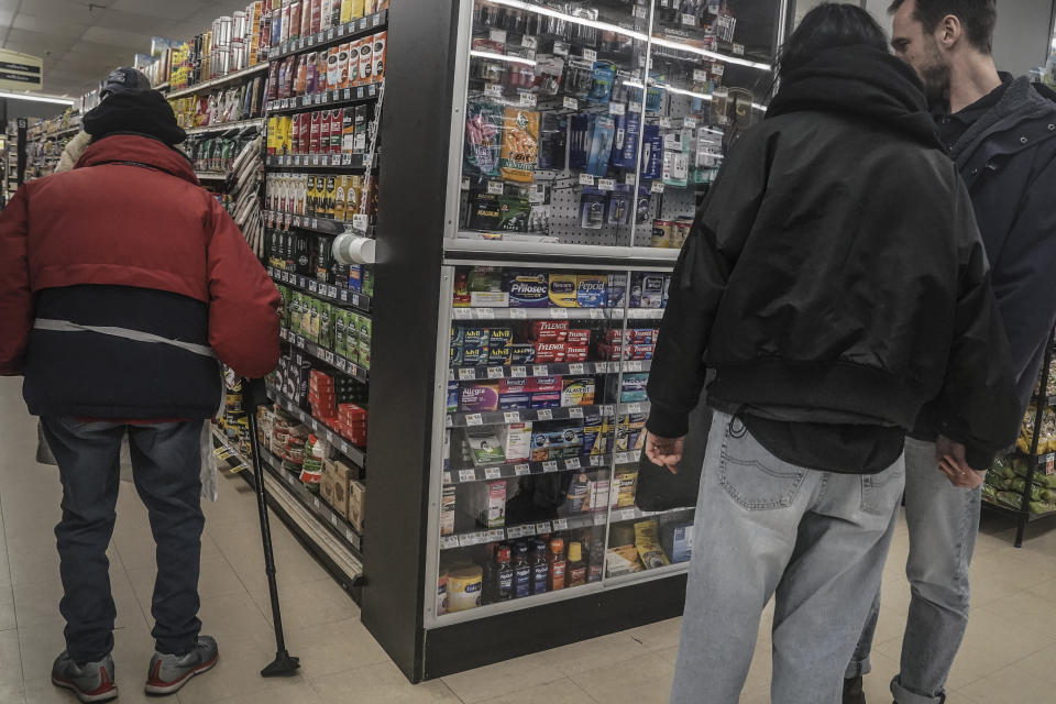 Shoppers browse pharmaceutical items locked in a glass cabinet at a Gristedes supermarket, Tuesday Jan. 31, 2023, in New York. Increasingly, retailers are locking up more products or increasing the number of security guards at their stores to curtail theft. (AP Photo/Bebeto Matthews)