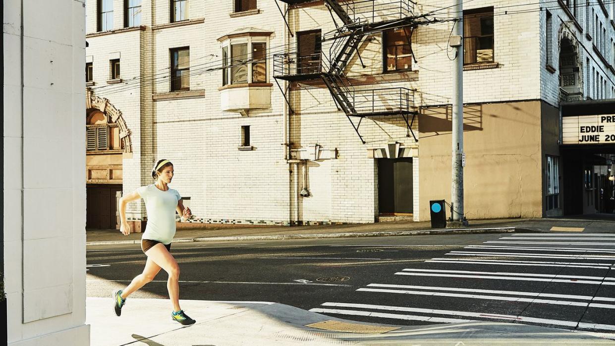 Pregnant woman running on city sidewalk during early morning workout