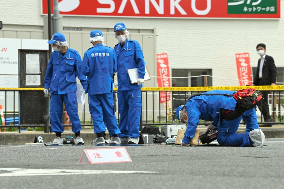 Officers investigate the site where former PM Shinzo Abe was shot while making a speech in front of Yamatosaidaiji Station on 8 July in Nara, Japan (The Asahi Shimbun via Getty)