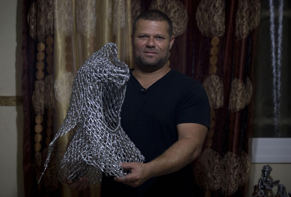 In this Saturday, Nov 2, 2019 photo, Palestinian artist Haitham Khateeb holds his sculpture depicting the late Palestinian leader, Yasser Arafat, with his famous keffiyeh, at his house in the West Bank village of Bilin near Ramallah. After 14 years as a photographer in the Israeli-occupied West Bank, Khateeb has found his second calling through sculpture, telling stories by recycling metal wire into art. (AP Photo/Majdi Mohammed)