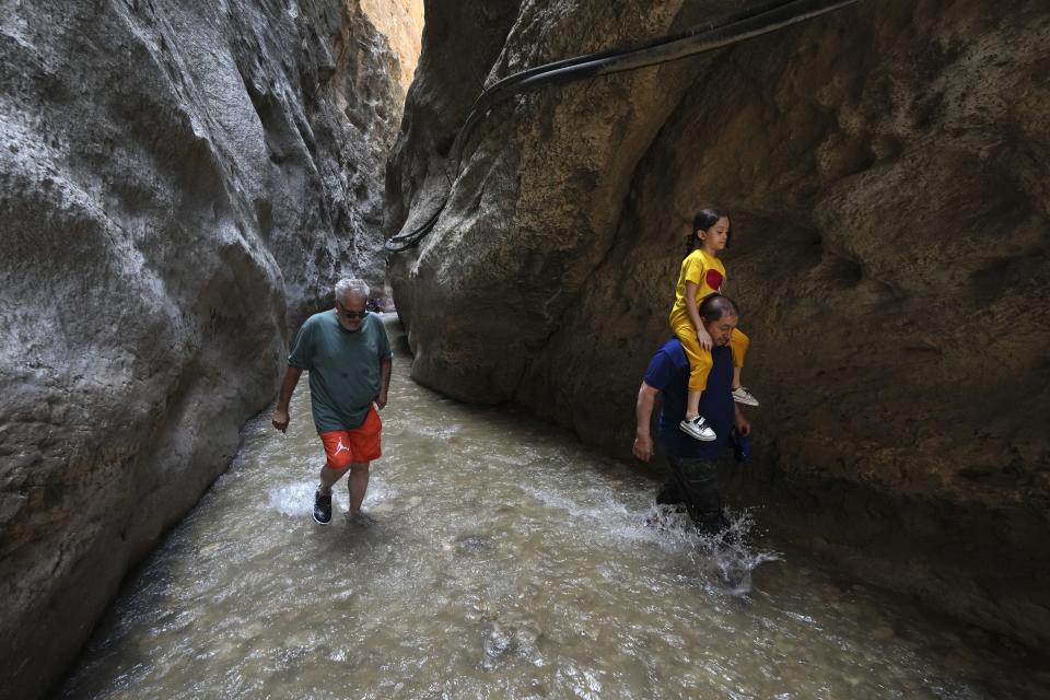 People walk in a cold mountain river streaming through Tangeh Vashi canyon north of the capital Tehran, Iran, Wednesday, July 19, 2023. (AP Photo/Vahid Salemi)