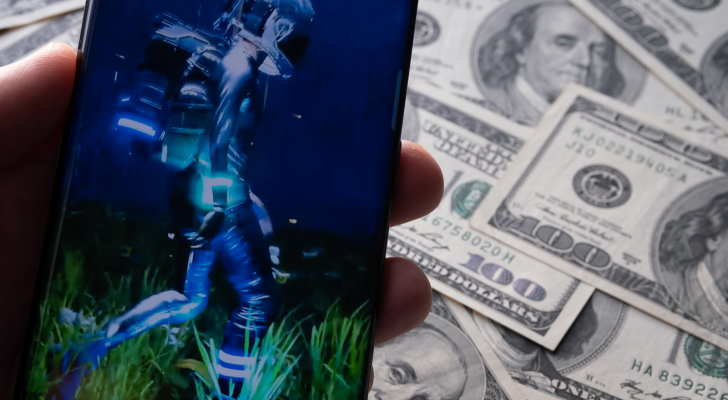 Beeple's 'HUMAN ONE' NFT stop frame image seen on smartphone and dollar bills seen on blurred background