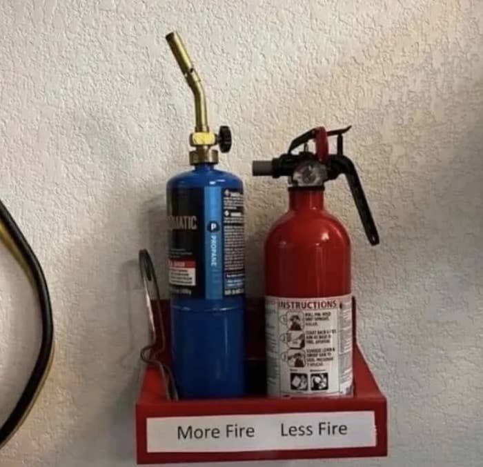 A propane tank and fire extinguisher are sitting right next to each other on the same shelf, labeled "more fire" and "less fire," respectively