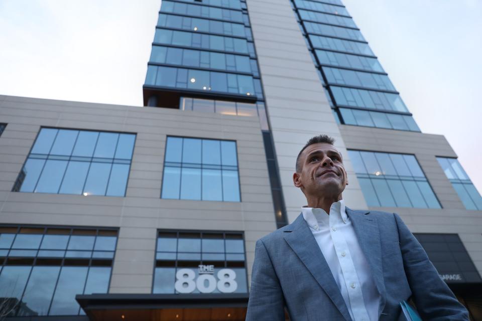 Troy Marr standing in front of a glass-windowed skyscraper that has the name The 808 on the side.