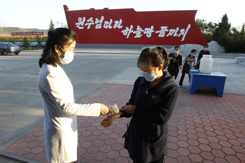 Hygienic and anti-epidemic officials disinfect and check the temperature of people outside the entrance to Songdowon General Foodstuff Factory in the city of Wonsan, Kangwon Province, North Korea DPRK, on Wednesday, Oct., 28, 2020. (AP Photo/Jon Chol Jin)