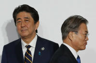 FILE - In this June 28, 2019, file photo, South Korean President Moon Jae-in, right, walks by Japanese Prime Minister Shinzo Abe upon his arrival for a welcome and family photo session at the G-20 leaders summit in Osaka, western Japan. South Korea said Thursday, Aug. 22, it is canceling an intelligence-sharing pact with Japan amid a bitter trade dispute, a surprise announcement that is likely to set back U.S. efforts to bolster mutual security cooperation with two of its most important allies in the Asian region. (Kim Kyung-Hoon/Pool Photo via AP, File)