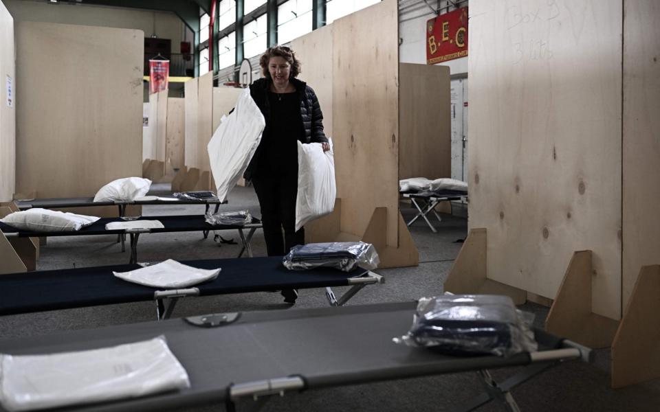 A woman places pillows on beds in a public gymnasium being prepared for Ukrainian refugees in Bordeaux, southwestern France, on March 25, 2022.  - Philippe Lopez/AFP