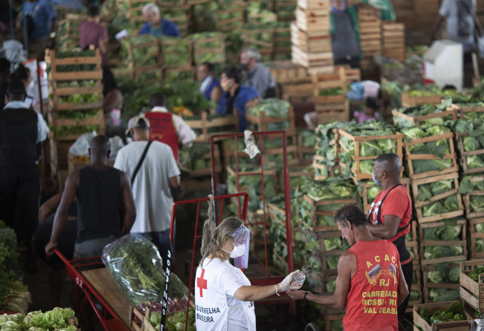 A member of the Red Cross hands out disinfectant to a worker at the wholesale market CEASA, amid the new coronavirus pandemic, in Rio de Janeiro, Brazil, Tuesday, June 23, 2020. Evidence is mounting that these types of markets contributed to the spread of COVID-19 in Latin America. (AP Photo/Silvia Izquierdo)