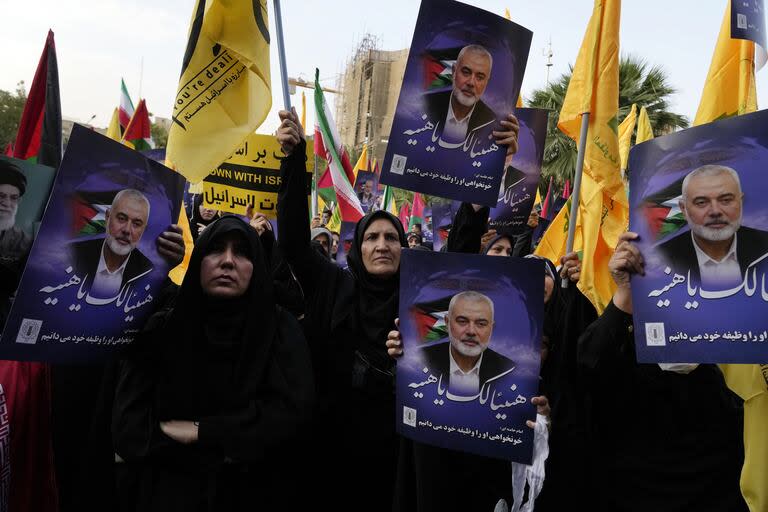 Manifestantes iraníes asisten a una manifestación para condenar el asesinato del líder de Hamás Ismail Haniyeh mientras sostienen sus carteles con letreros que dicen en árabe: 