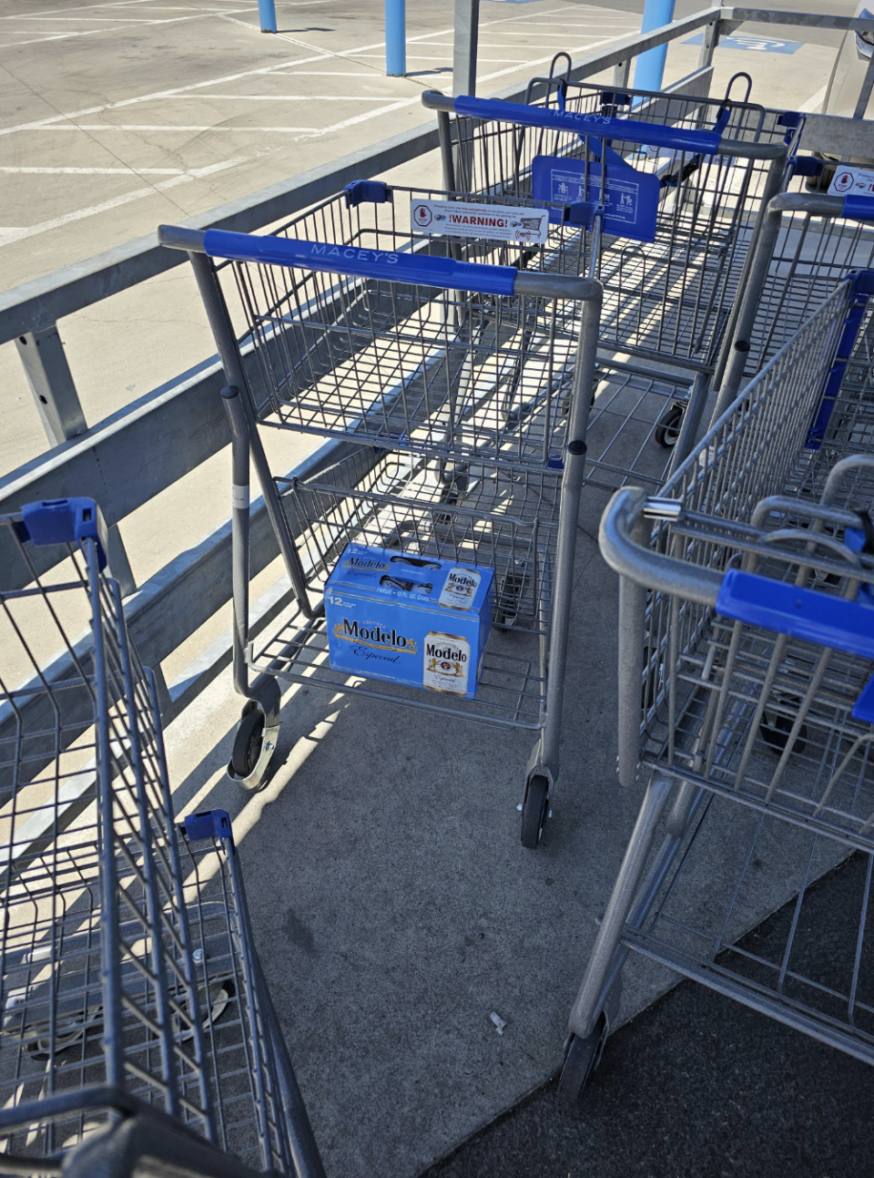 Shopping carts in a parking lot, one of them with a cardboard box of Modelo beer