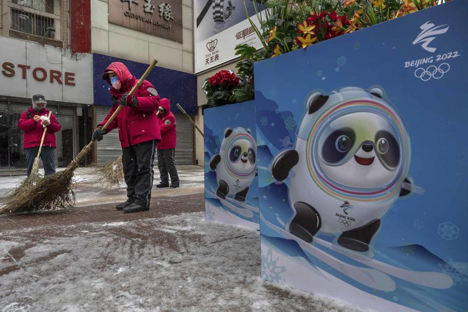 2022年1月20日北京，志願者在北京冬奧會和殘奧會海報旁邊掃雪，海報展示了吉祥物「冰墩墩」。