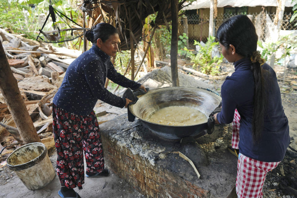 Chin Ith, left, adjusts a vessel of palm sap onto a fire to make palm sugar at Trapang Ampel village, outside Phnom Penh, Cambodia, Friday, March 15, 2024. (AP Photo/Heng Sinith)