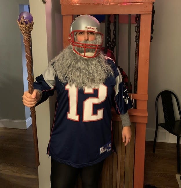 A woman in a football uniform with a long gray beard and a staff stick