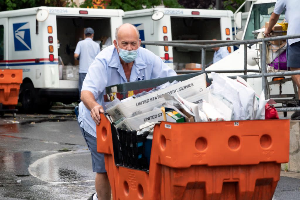 A postal office workers loads a cart around with letters to post office trucks. 