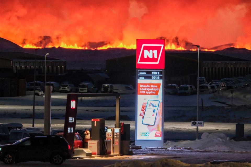 People fill up their vehicles at a petrol station as lava and billowing smoke pours out of a fissure during a volcanic eruption near Grindavík, in western Iceland, on Feb. 8, 2024.<span class="copyright">Kristinn Magnusson—AFP/Getty Images</span>