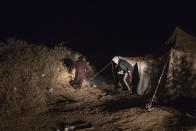 Smugglers walk past a tent that is used while building fishing boats intended to carry migrants to the Canary Islands, in a remote desert out of the town of Dakhla, in Morocco-administered Western Sahara, Tuesday, Dec. 22, 2020. (AP Photo/Mosa'ab Elshamy)