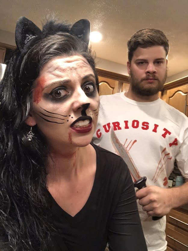 A woman dressed as a bloody cat and a man with a knife wearing a shirt that says "curiosity" 