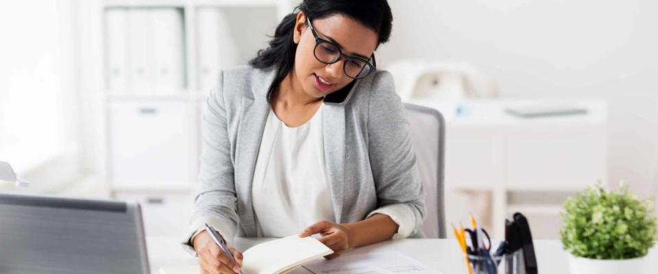 happy businesswoman or secretary with notebook calling on smartphone at office