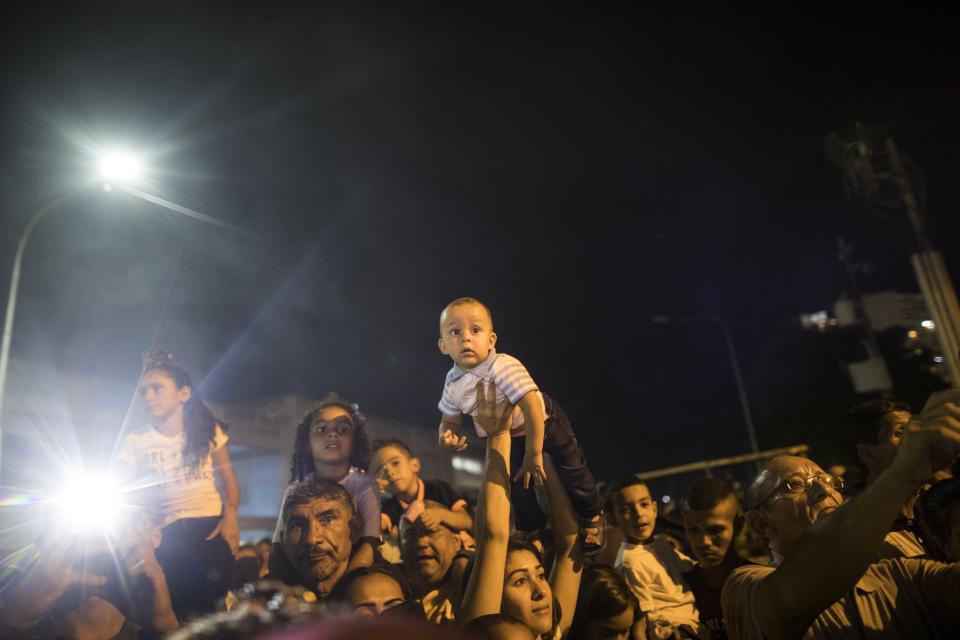 In this Nov. 18, 2019 photo, faithful hold up their kids so they can get a glimpse of the image of the Virgin of Chiquinquira, also called La Chinita, during a procession in Maracaibo, Venezuela. Thousands of Venezuelans flocking to Maracaibo’s ornate basilica each year at this time traditionally ask for help overcoming illness or conceiving a child. But many faithful say a crisis driving the exodus of millions has made them ask for something bigger than themselves. (AP Photo/Rodrigo Abd)