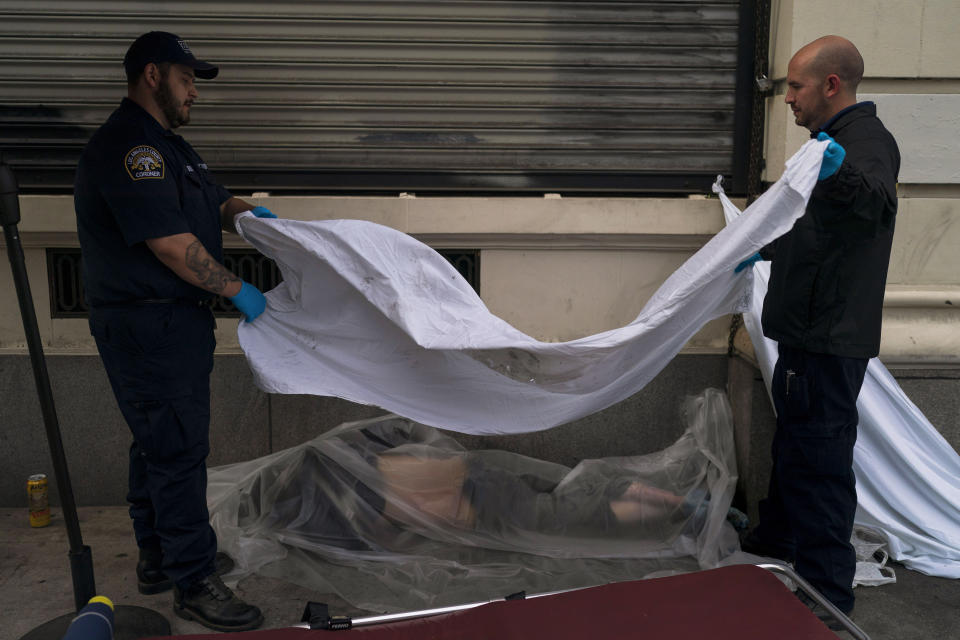 Forensic assistant Laurentiu Bigu, left, and investigator Ryan Parraz from the Los Angeles County coroner's office cover the body of a homeless man found dead on a sidewalk in Los Angeles, Monday, April 18, 2022. The 60-year-old man died from the effects of methamphetamine, according to his autopsy report. Nearly 2,000 homeless people died in the city from April 2020 to March 2021, a 56% increase from the previous year, according to a report released by the Los Angeles County Department of Public Health. Overdose was the leading cause of death, killing more than 700. (AP Photo/Jae C. Hong)