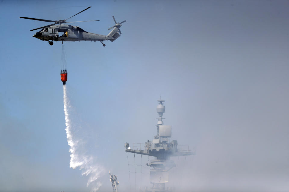 A helicopter drops water on the USS Bonhomme Richard Monday, July 13, 2020, in San Diego. Fire crews continue to battle the blaze Monday after 21 people suffered minor injuries in an explosion and fire Sunday on board the USS Bonhomme Richard at Naval Base San Diego. (AP Photo/Gregory Bull)