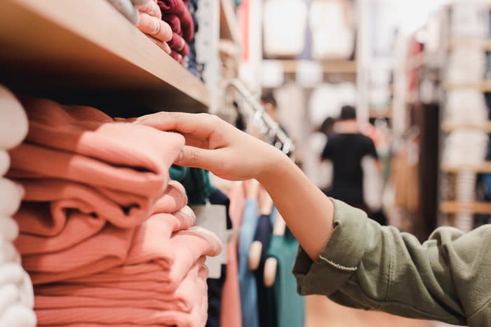 A person reaches for a shirt on a shelf in a clothing store.
