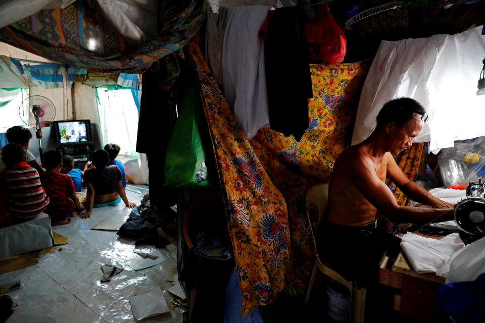 Abdul Gani, 49, works with a sewing machine as his children and nephews watch TV in a tent at an evacuation camp for families displaced by the Marawi siege, in Marawi City, Lanao del Sur province, Philippines. (Photo: Eloisa Lopez/Reuters)