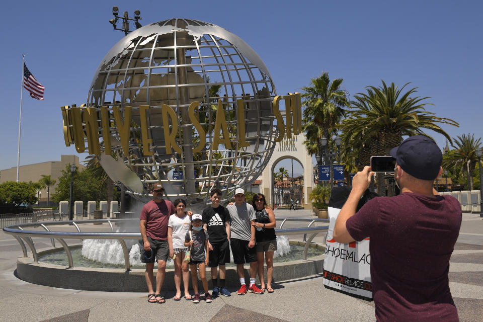 A family has their picture taken at Universal CityWalk, Thursday, June 11, 2020, near Universal City, Calif. The tourist attraction, which had been closed due to the coronavirus outbreak recently re-opened. The Universal Studios tour is still closed. (AP Photo/Mark J. Terrill)