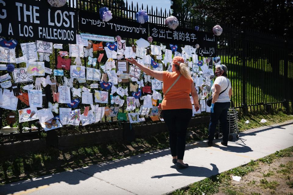 People walk by a memorial for those who have died from the coronavirus outside Green-Wood Cemetery on May 27, 2020, in the Brooklyn borough of New York City. Green-Wood Cemetery, one of New York's oldest cemeteries, has been the site of hundreds of burials and cremations of COVID-19 victims.