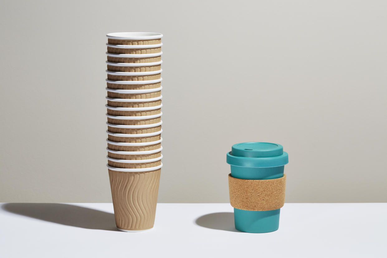 A stack of disposable coffee cups next to a reusable coffee cup