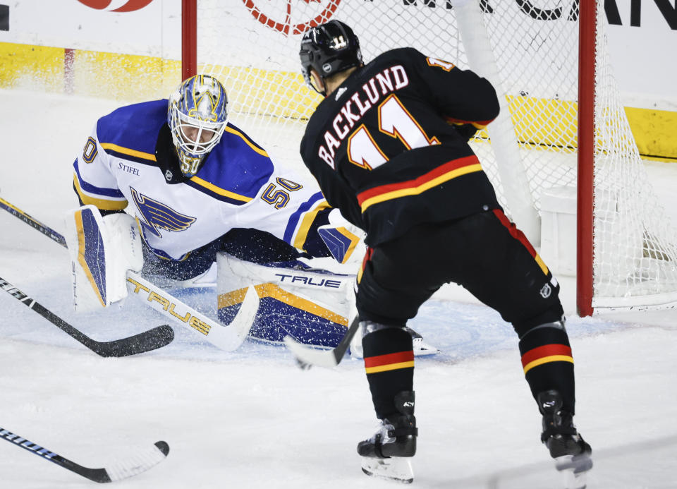 St. Louis Blues goalie Jordan Binnington (50) lunges to stop a shot from Calgary Flames forward Mikael Backlund (11) during the second period of an NHL hockey game in Calgary, Alberta, Tuesday, Jan. 23, 2024. (Jeff McIntosh/The Canadian Press via AP)